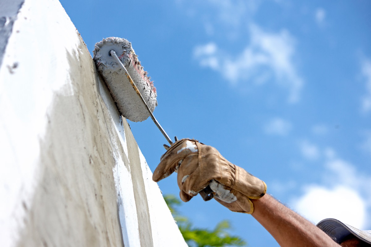 builder worker painting facade of high rise building with roller